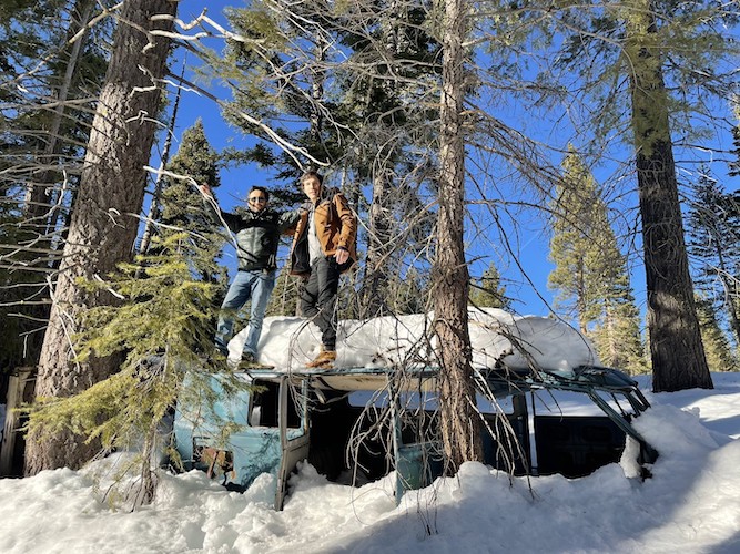 Diego and Tomas standing on a car in the forest.