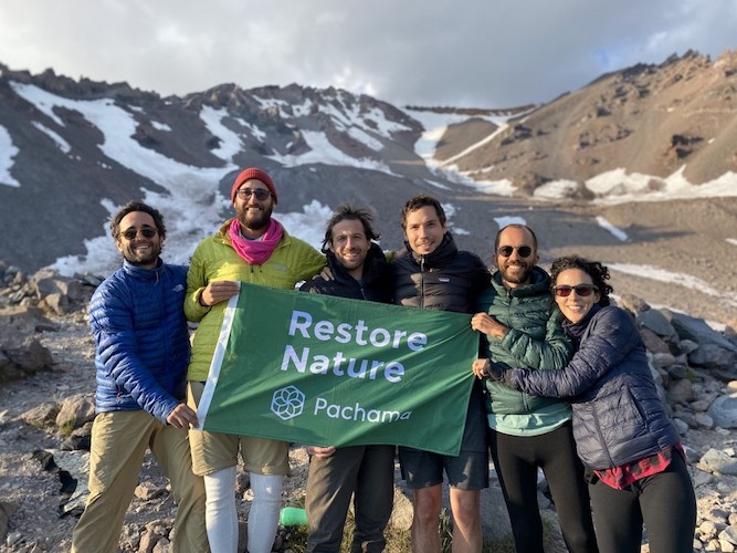 Team huddling on top of mountain with Pachama flag